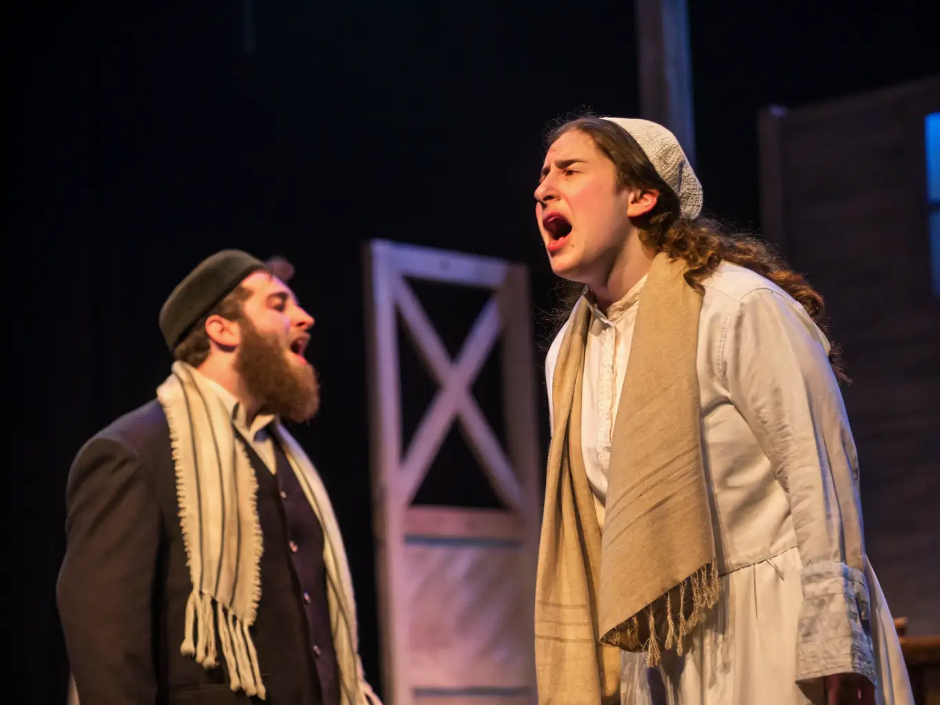 A visually appealing image showcasing a Yiddish theater performance, with actors in costume on stage, delivering a dramatic scene. The backdrop is a traditional Yiddish setting, and the audience is captivated by the performance.